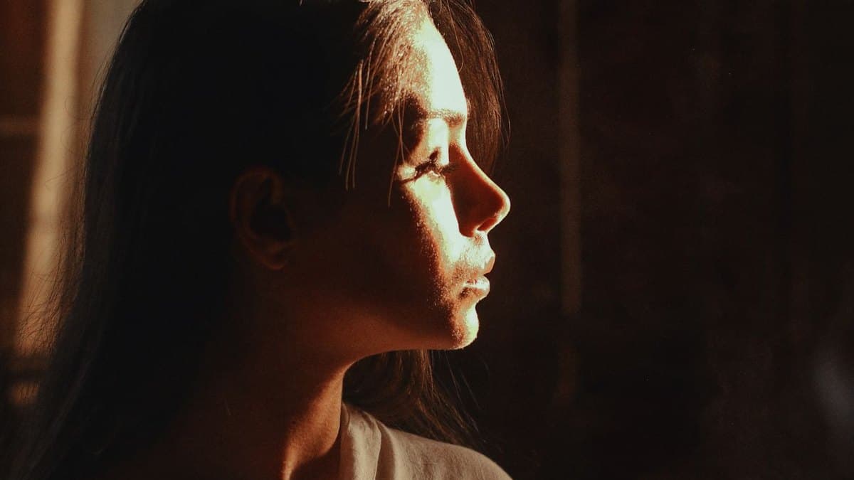Profil d'une femme éclairé par une lumière douce, les yeux baissés